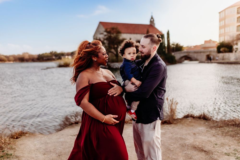 Expectant couple shares a tender moment on a beach at sunset with a church building in the background.