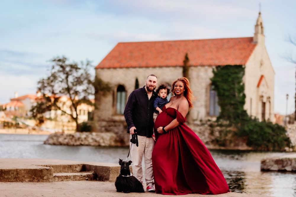 Golden sunset illuminates couple posing at a charming stone chapel with red dress against rustic architecture.