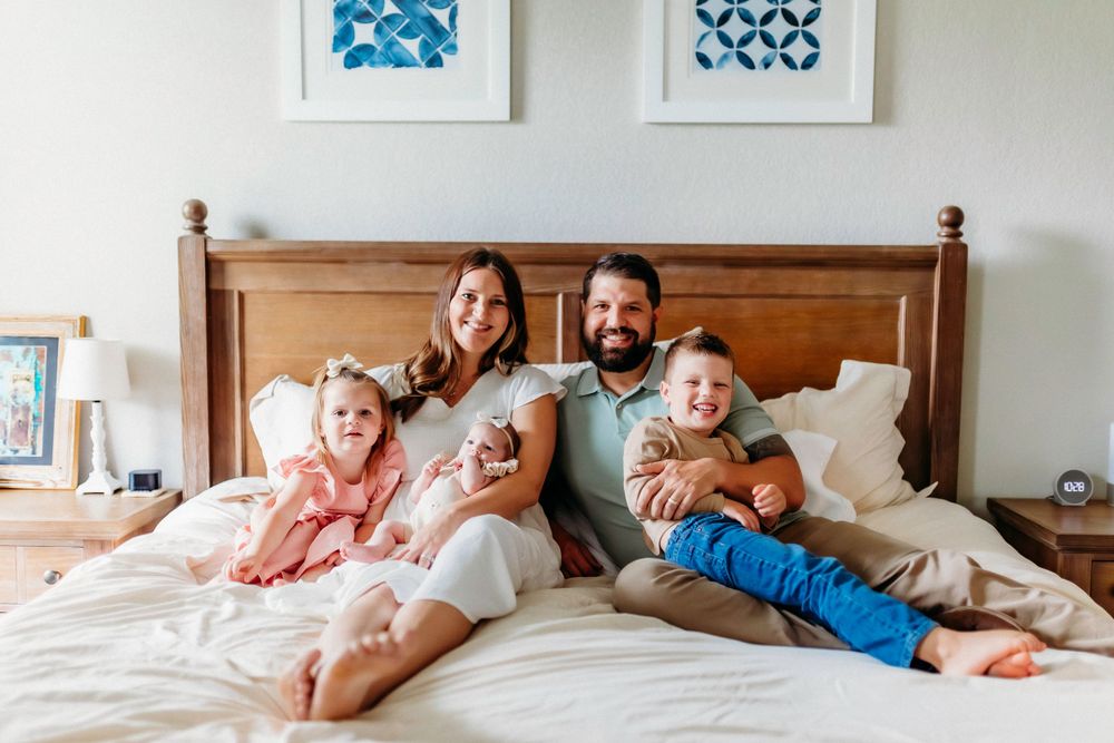 Family lounging together on bed with wooden headboard and blue wall art.