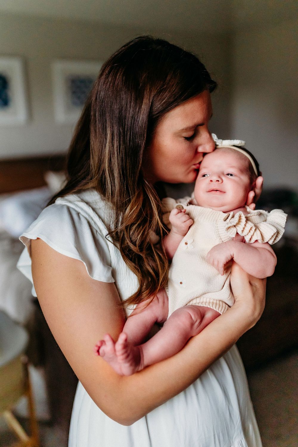 A tender moment between a mother and newborn baby as she kisses her infant's cheek in a softly lit room.