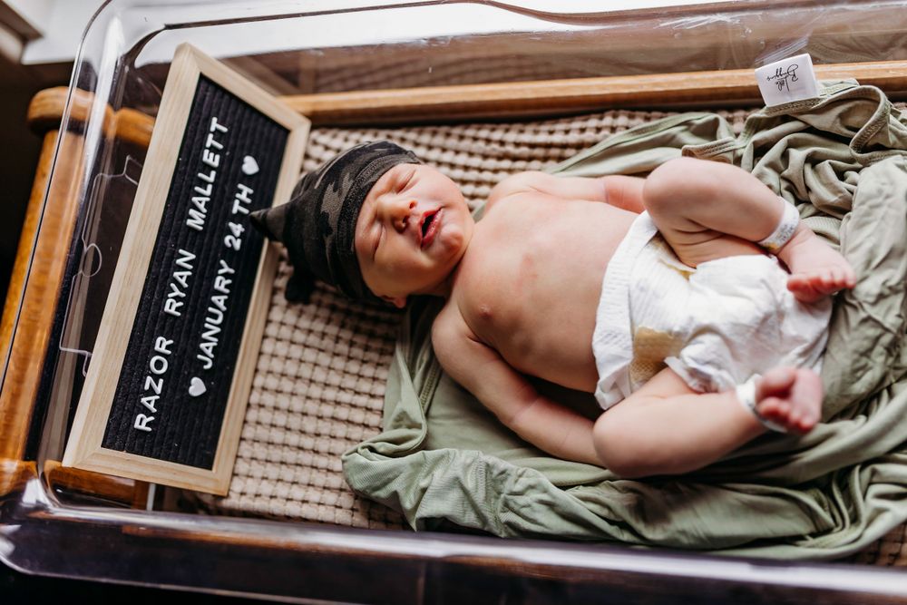 Newborn baby lying on textured blanket next to identification card in hospital.
