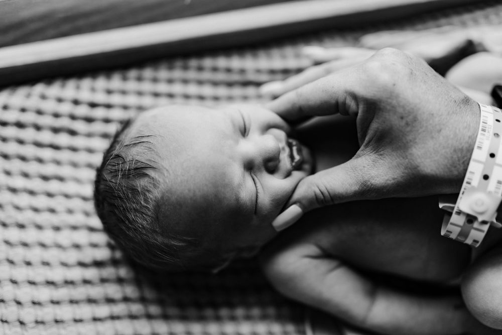 Black and white portrait of newborn baby showing genuine emotion during first moments of life.