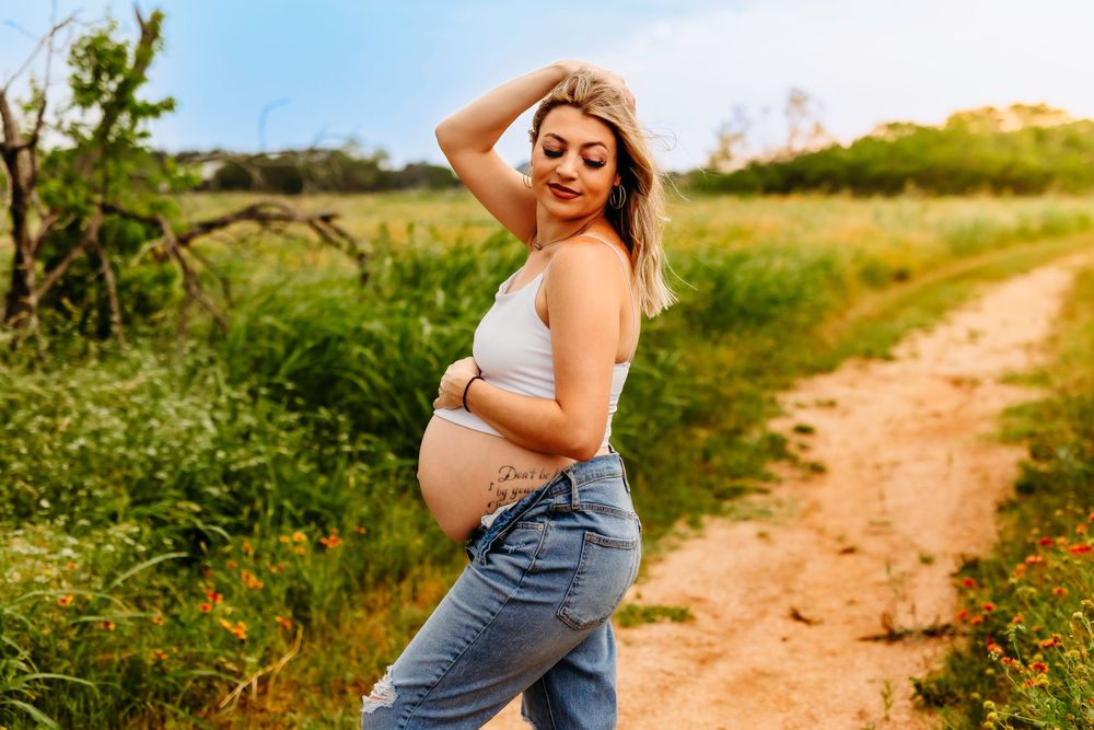 Expecting mother in casual denim poses on sunny dirt path.