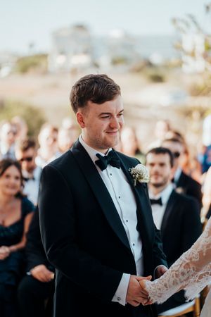 A groom in a black tuxedo shares an emotional moment during an outdoor wedding ceremony.