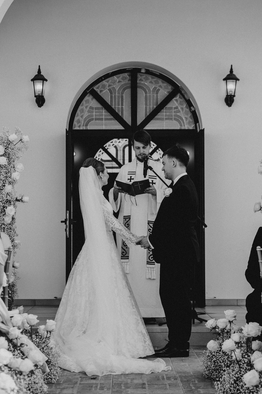 Black and white wedding photos show a sequence of romantic moments between a couple in front of an arched doorway.