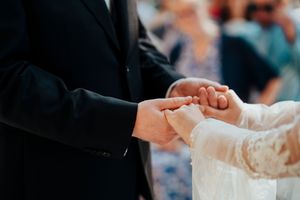 Bride and groom exchange rings during an elegant outdoor wedding ceremony with guests in attendance.
