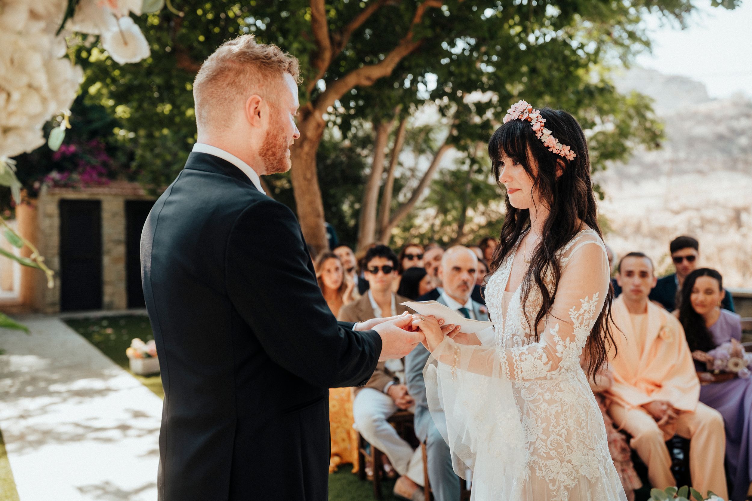 Wedding couple shares intimate moments during outdoor ceremony in garden setting with guests looking on.