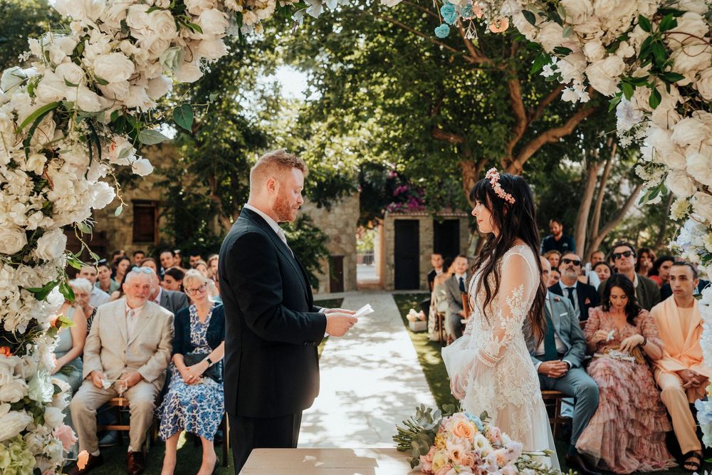 Wedding guests celebrate under a floral arch at an outdoor garden ceremony with white flower decorations.