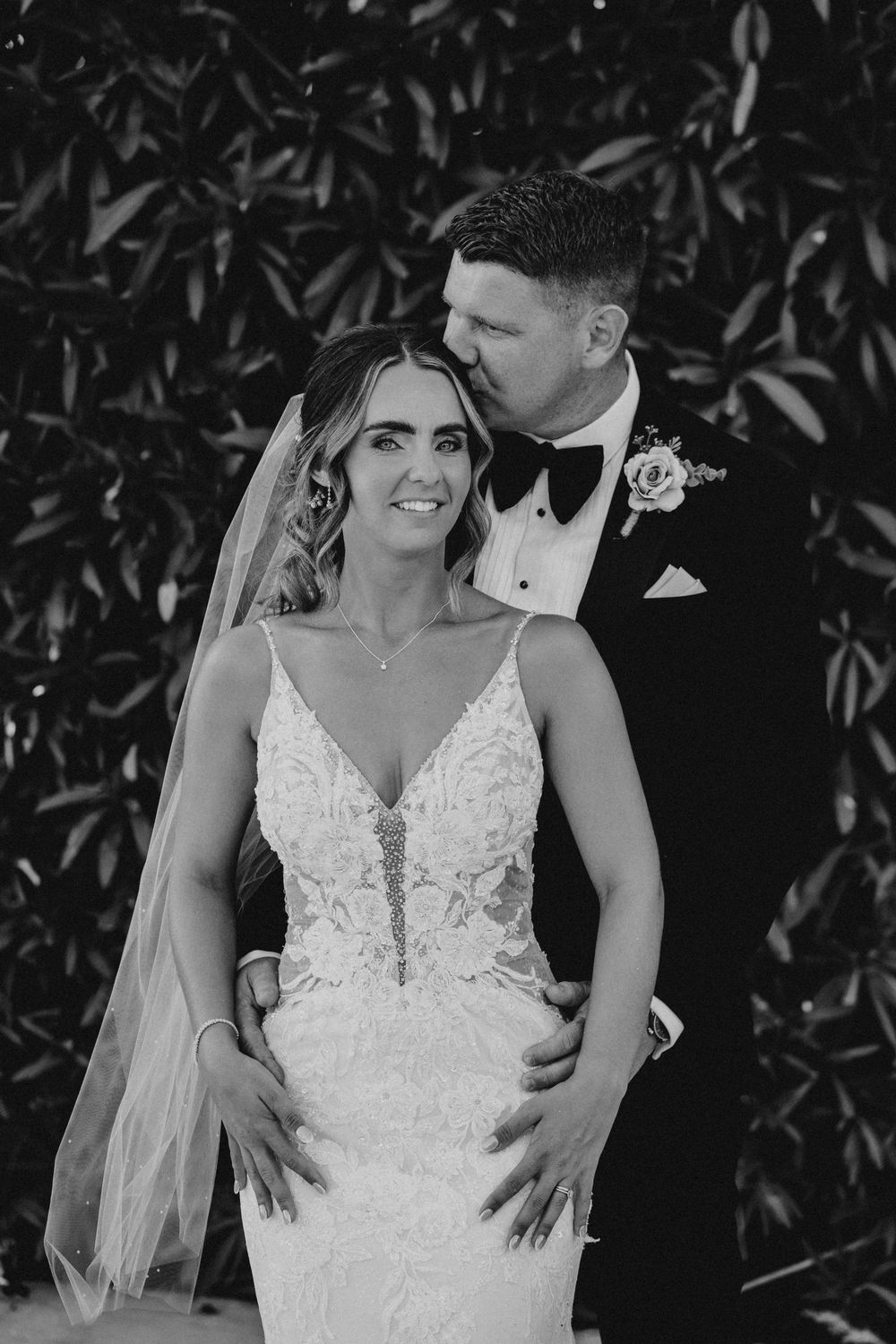 A romantic black and white wedding photo series showing intimate moments between newlyweds against a leafy backdrop.