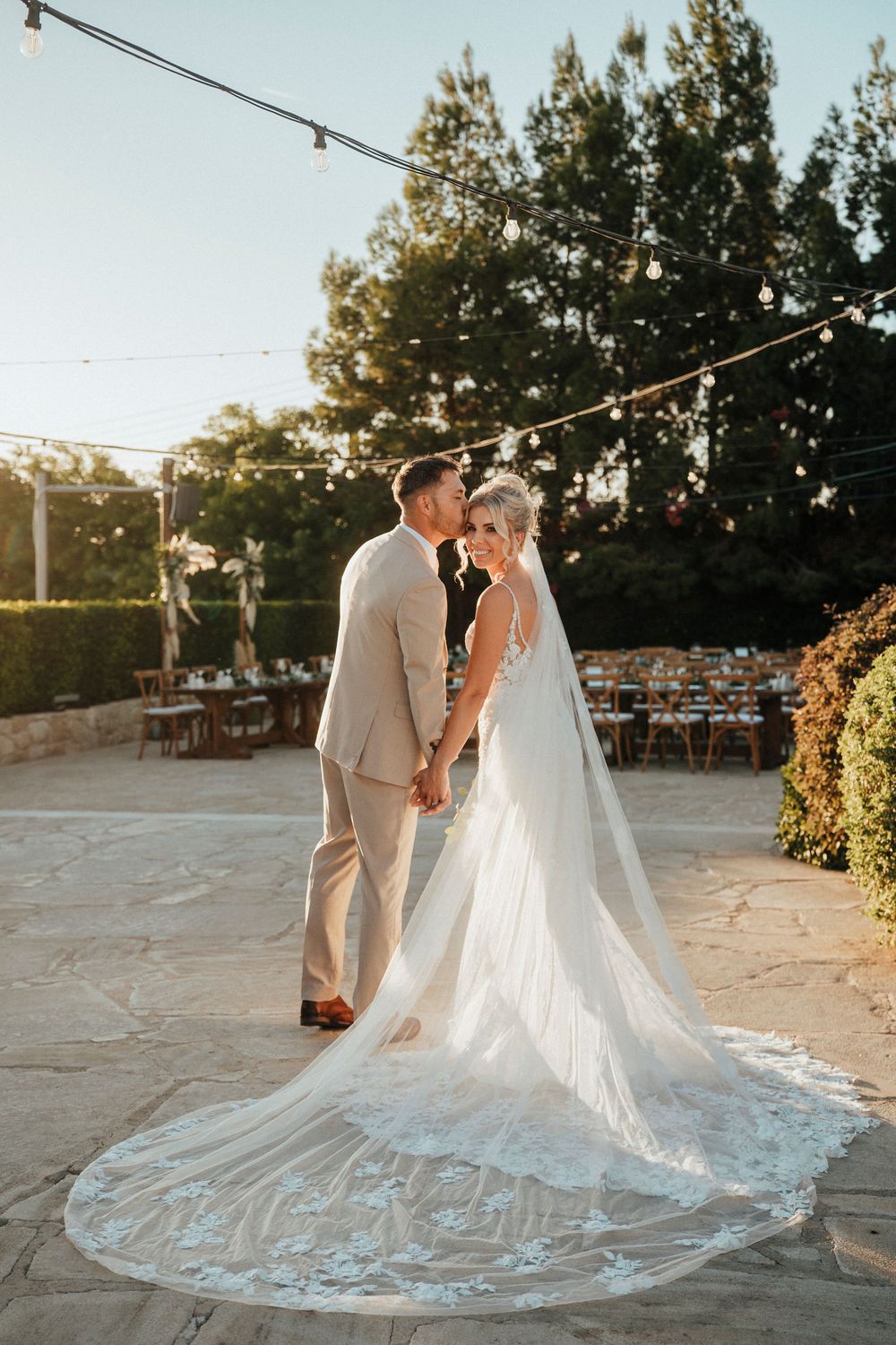 A couple shares an intimate moment at sunset with a stunning cathedral-length lace veil trailing behind them.