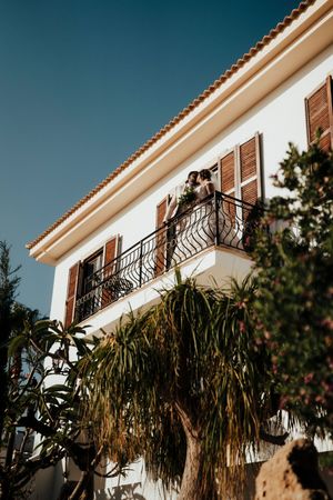 White stucco building with ornate black iron balconies and palm trees against a bright blue sky.