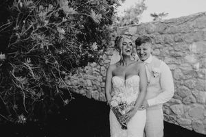 A couple shares a joyful moment together in front of a stone wall during a black and white photo session.