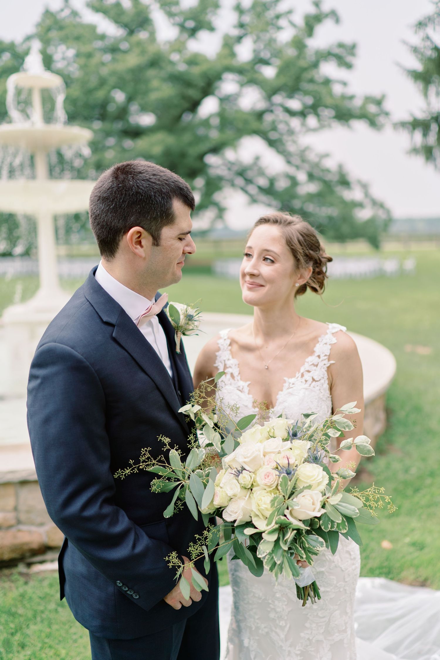Wedding portrait in front of garden fountain with lush floral bouquet.