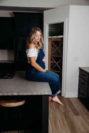 A person in a navy outfit sits casually on a kitchen counter in a modern home interior setting.