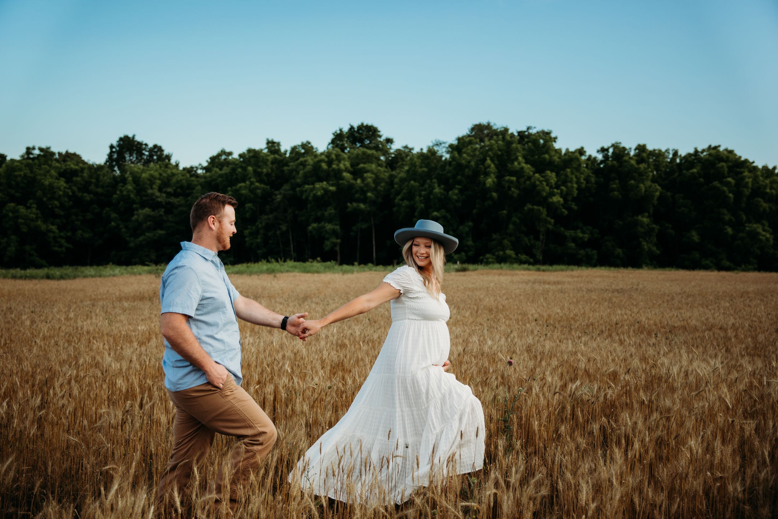 A couple in wedding attire stands together in a golden wheat field on a sunny summer day.