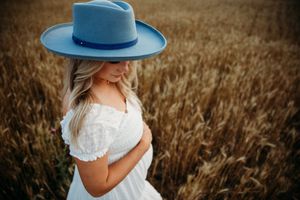 A romantic photoshoot in a golden wheat field with a blue hat and white dress creating a dreamy atmosphere.
