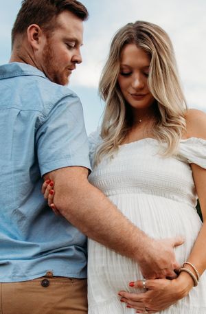 Couple in casual attire shares tender moments during maternity photoshoot against white background.