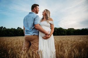 A couple shares an intimate moment together in a golden wheat field during sunset.