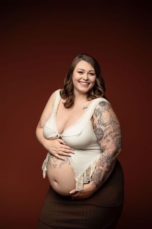 Maternity photo series showing pregnant person in white top and dark skirt against burgundy backdrop.