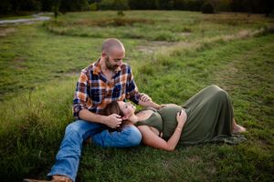 A couple lies together on green grass during a romantic outdoor photoshoot at sunset.