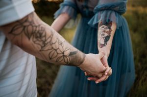 Close-up of tattooed hands holding each other against a teal dress background outdoors.