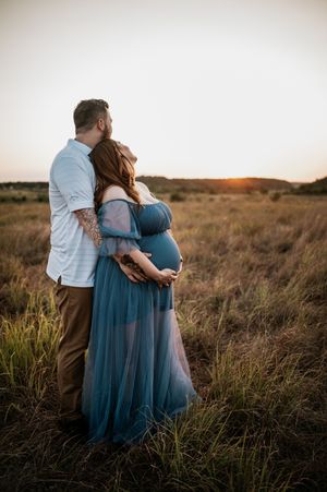 A couple embraces in a golden field at sunset wearing a blue dress and white shirt.
