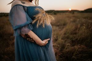 Couple in blue dress and white shirt embrace during sunset in rustic outdoor setting.