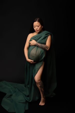 Artistic maternity portrait series showing a woman in flowing emerald green fabric against a dark background.