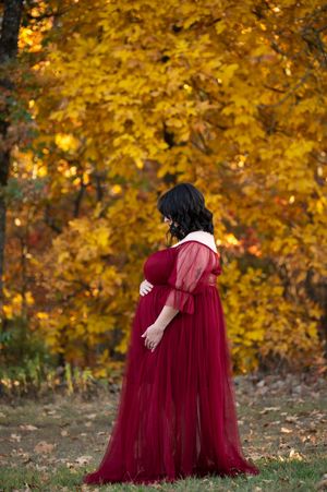 Two figures in flowing burgundy dresses embrace against a backdrop of golden autumn foliage.