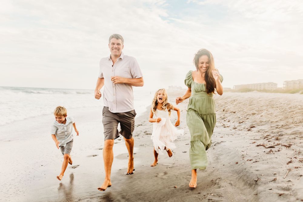 Family running together along beach shoreline at sunset.