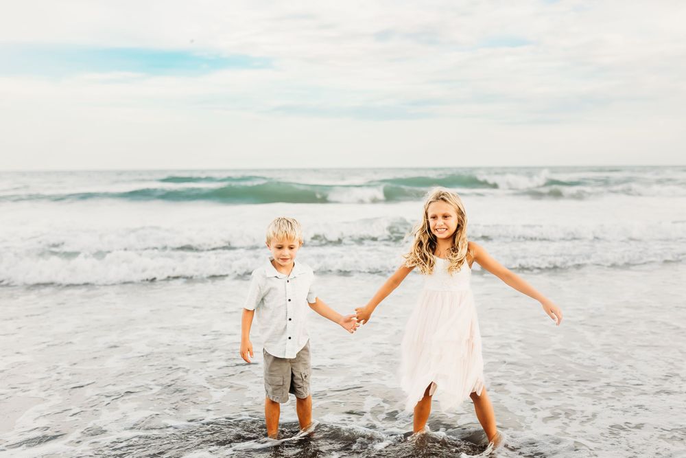 Two children playing and holding hands in ocean waves at beach.