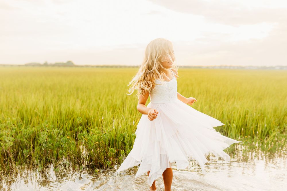 White dress twirling in grassy marsh field at sunset.