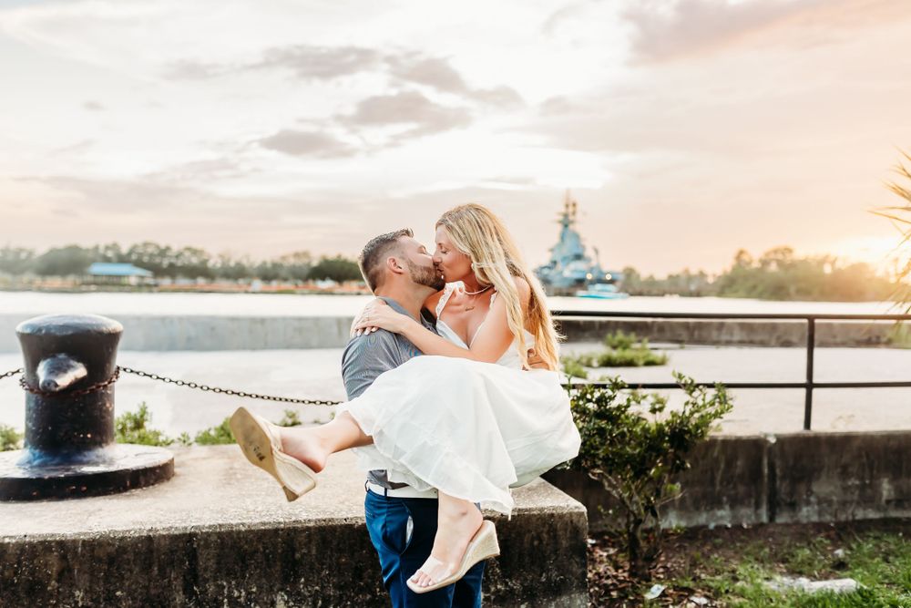 Romantic sunset portrait by waterfront with lighthouse in background.