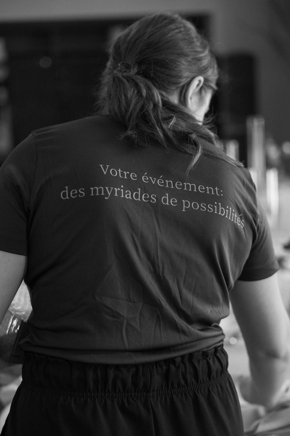 Back view of a person wearing a black t-shirt with French text reading votre evenement des myriades de possibilites.