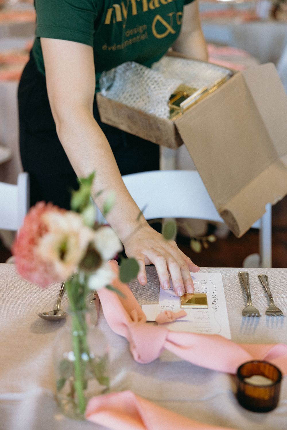 Event planner placing a menu card on an elegantly set table with pink floral arrangements and ribbon napkins.