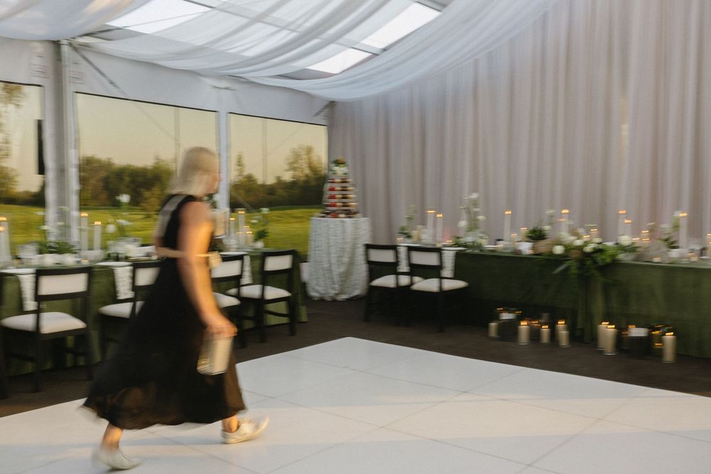 Wedding planner in black dress walking through a decorated tent reception venue with dance floor.