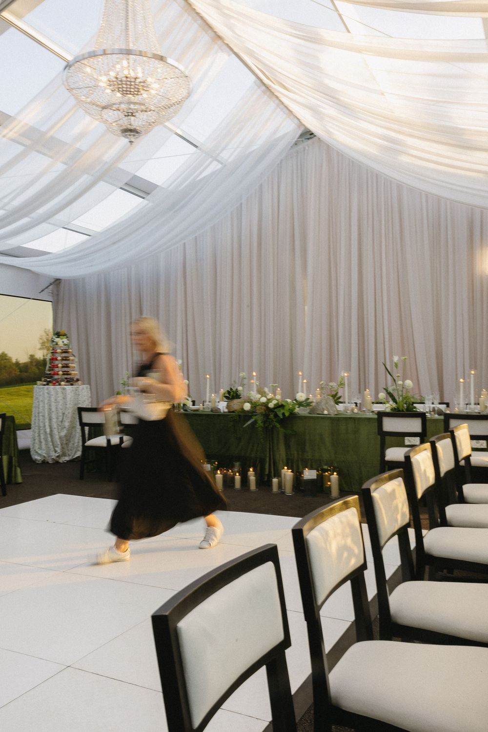 Motion blur photo of a wedding coordinator moving through an elegant tent reception with white dance floor.