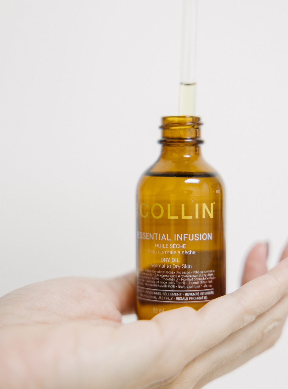 Hand holding a G.M. Collin Essential Infusion dry oil bottle against a clean white background.