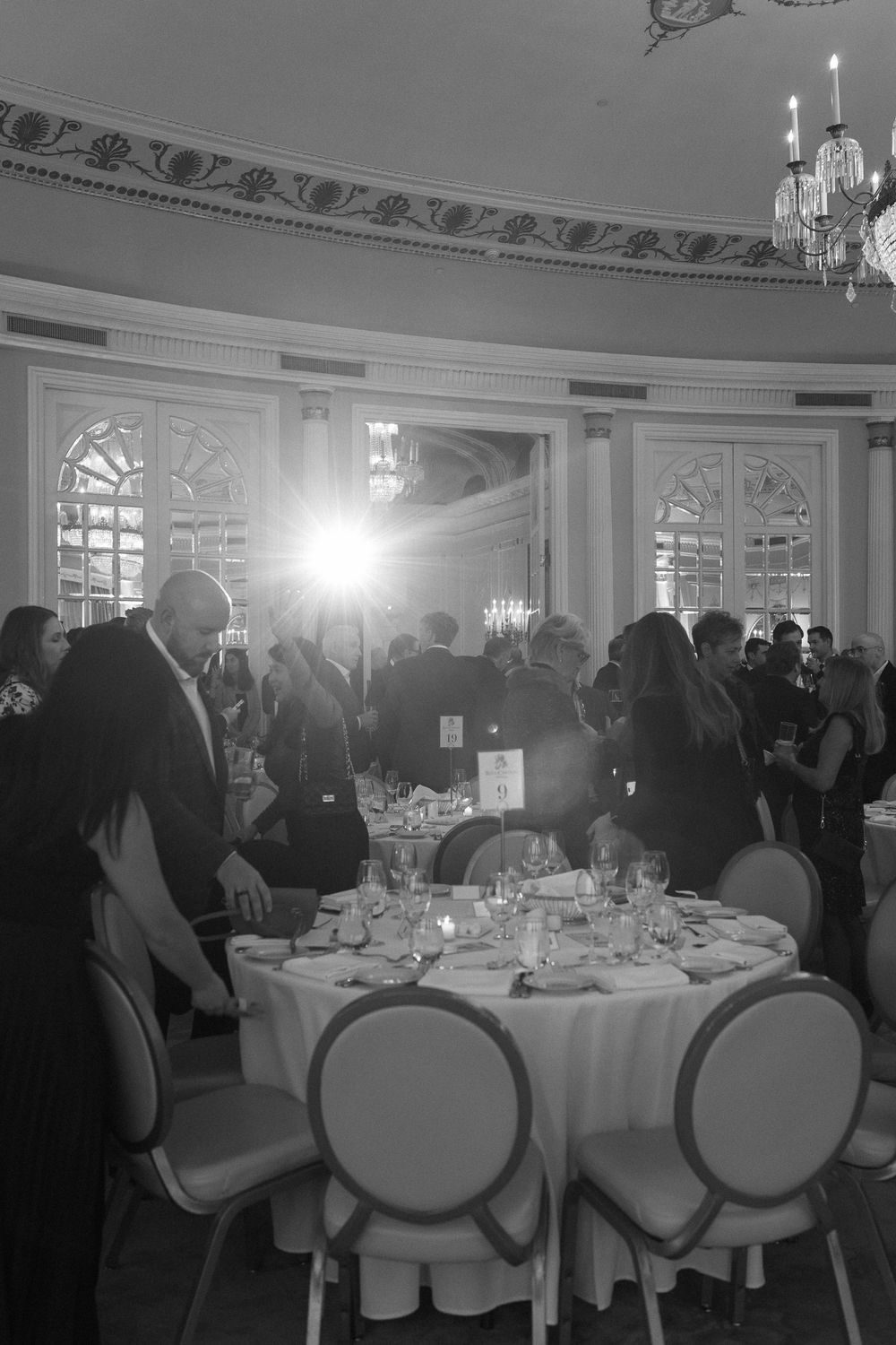 Black and white photo of elegant wedding reception in grand ballroom with chandelier lighting.