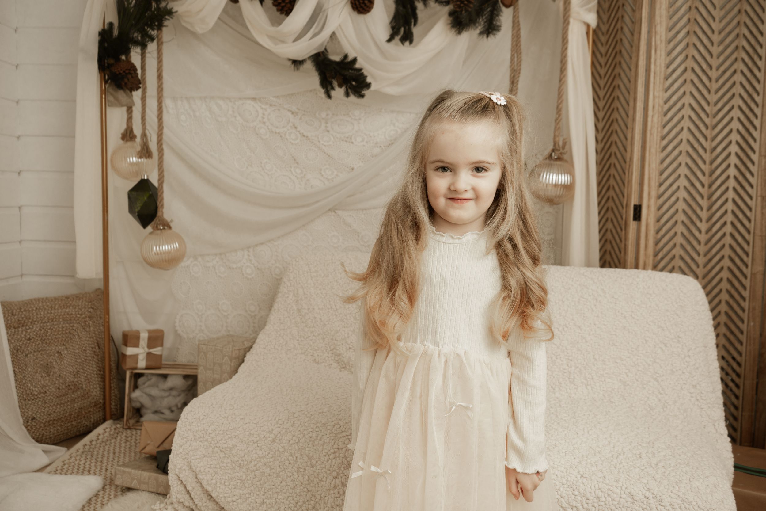 A child in a white dress stands in an elegant cream-colored room with ornate wall decorations and chevron wallpaper.