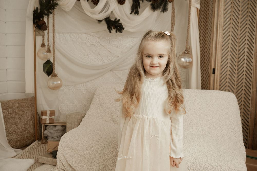A child in a white dress stands in an elegant cream-colored room with ornate wall decorations and chevron wallpaper.