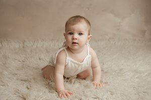 Baby in white outfit crawling on plush fur rug during professional portrait session.