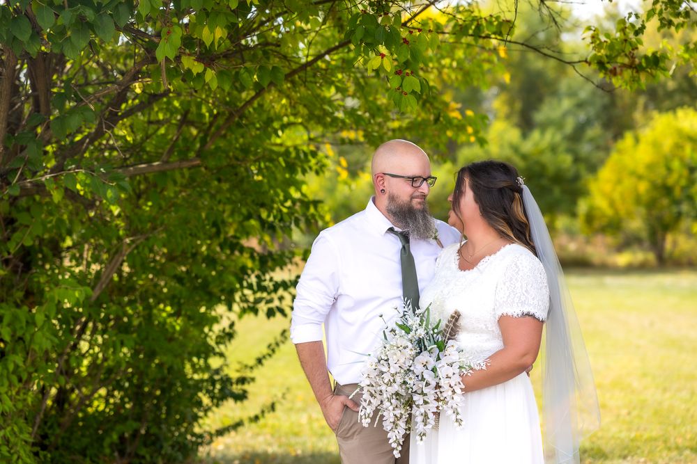 Romantic couple shares tender moment in sunlit meadow surrounded by lush green trees during golden hour.