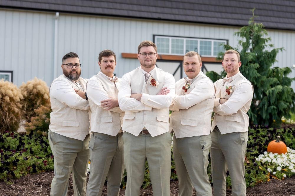 A group in matching cream colored suits and brown pants pose together in an outdoor garden setting.