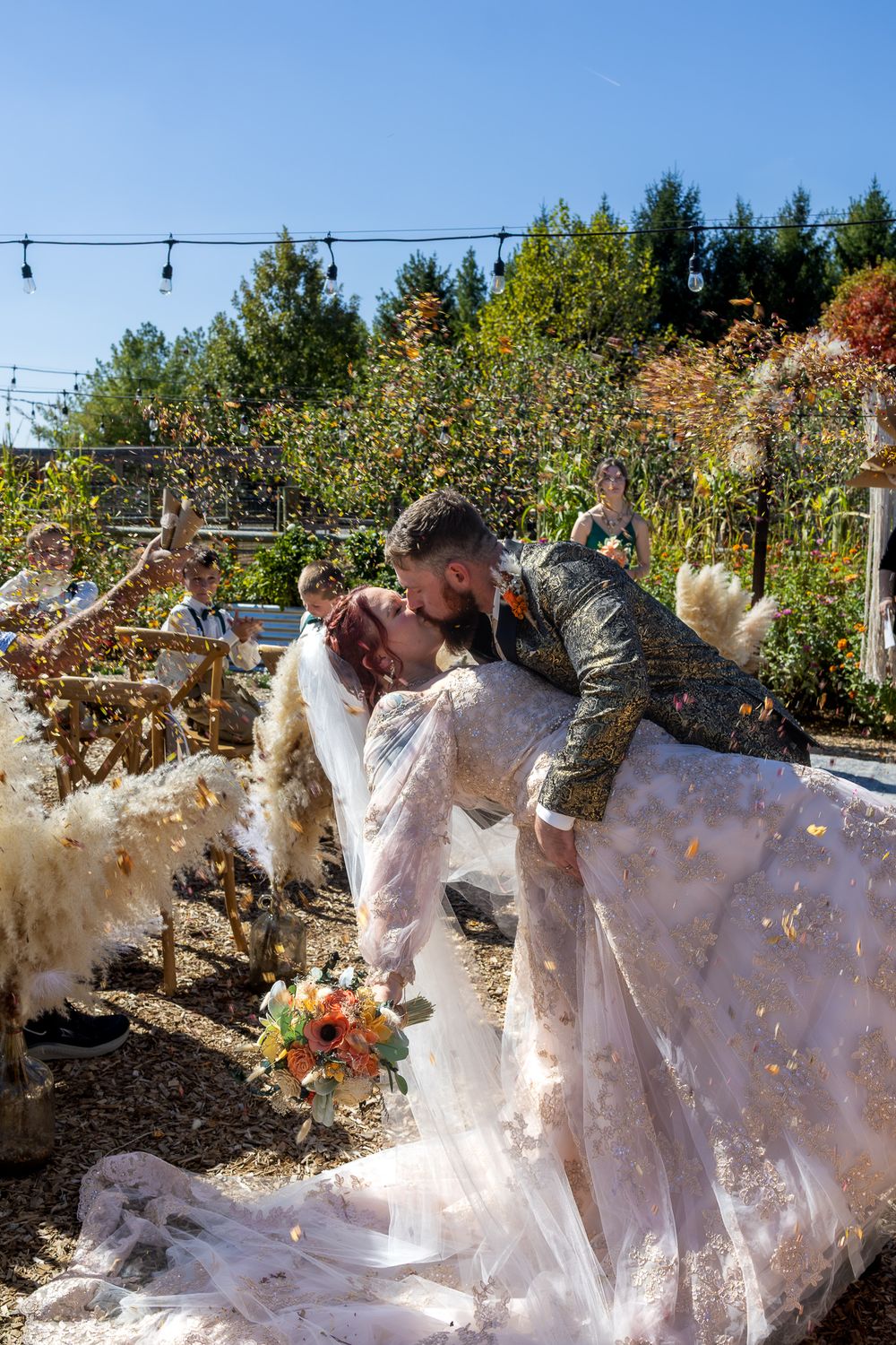 A series of white fabric ghost decorations with autumn leaves swirling around them displayed in an outdoor garden setting.