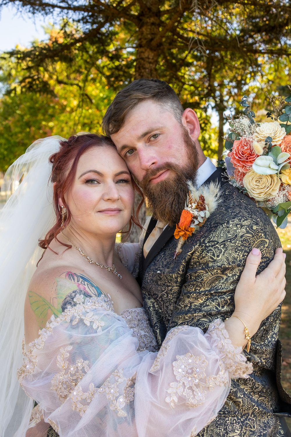A bride and groom embrace outdoors during an autumn wedding, with fall foliage and floral details visible.