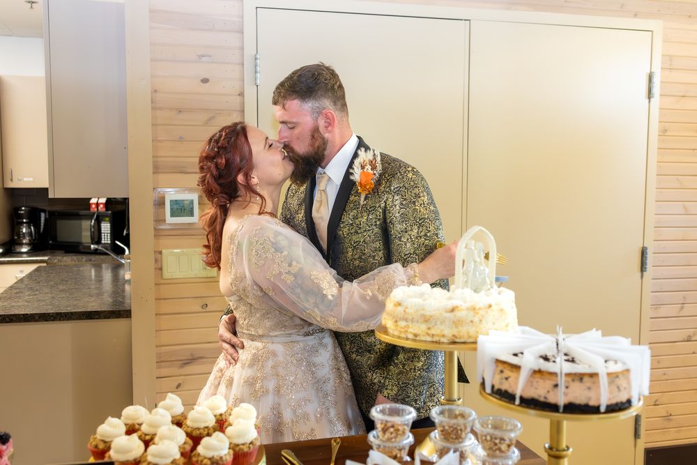 A wedding cake cutting scene with guests watching in a rustic wooden interior setting.