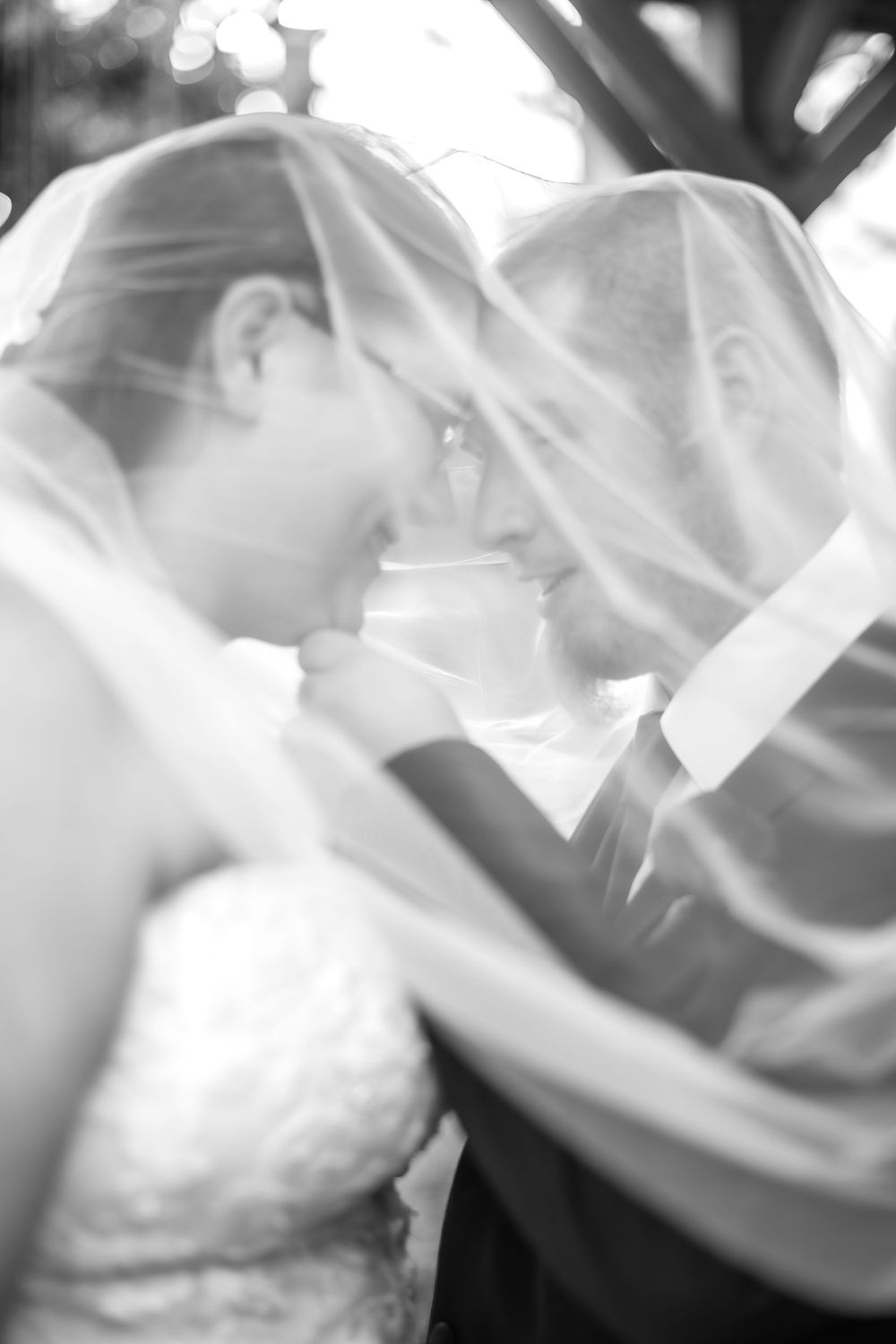 Black and white romantic wedding photo of couple sharing intimate moment under bridal veil.