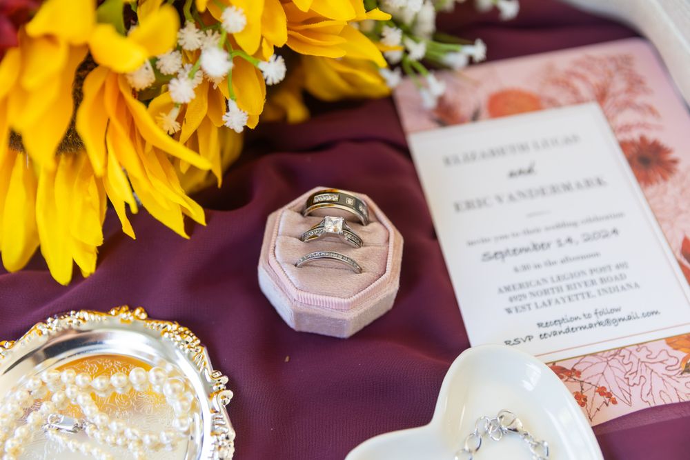 Wedding rings rest in a pink hexagonal box alongside sunflowers and invitation details.