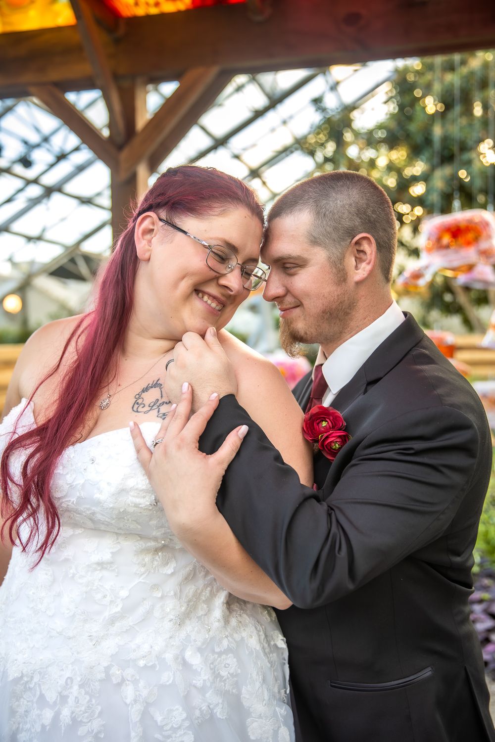 A romantic moment between newlyweds in formal attire under greenhouse lighting.